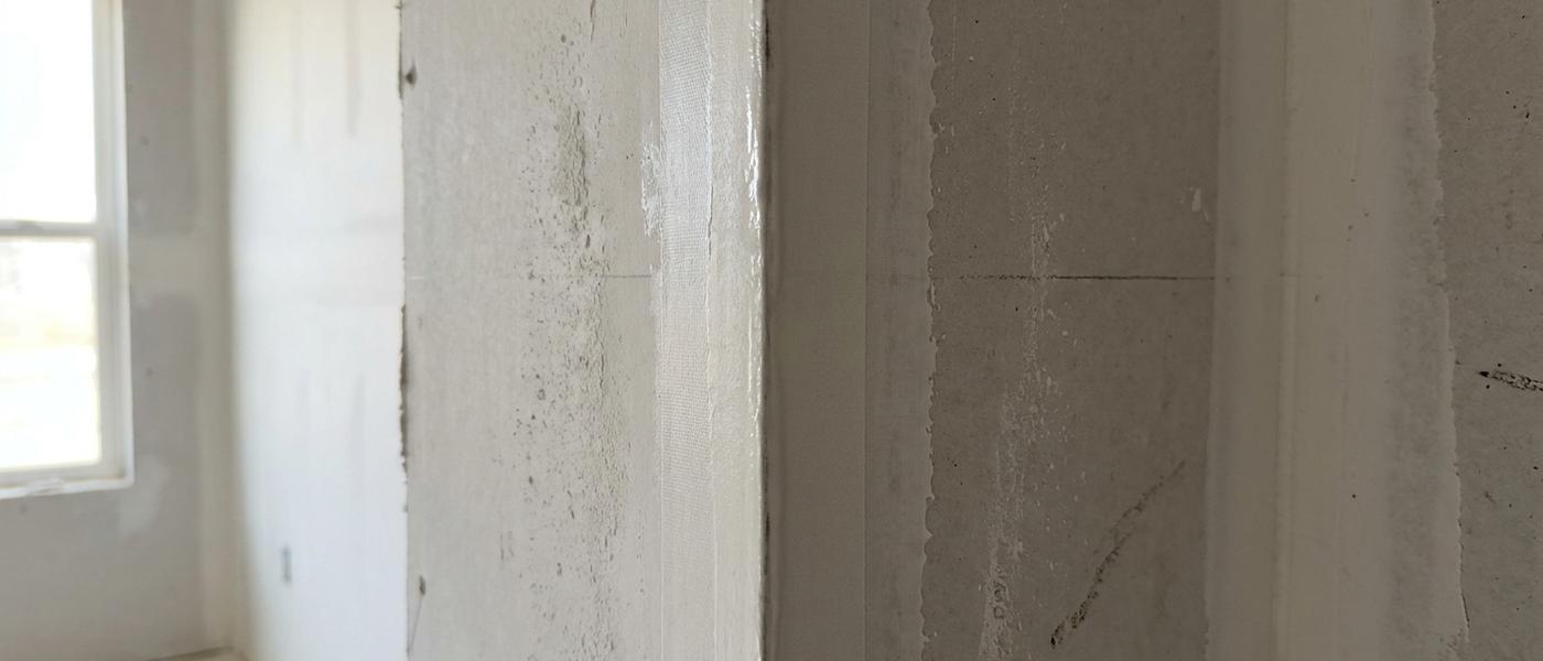 An inside corner in an unfinished room where the drywall joint has been taped with paper tape folded into the corner and coated with joint compound on both sides
