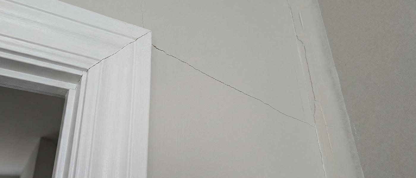 A fine crack running diagonally up from the top corner of a painted interior door frame across a smooth drywall wall